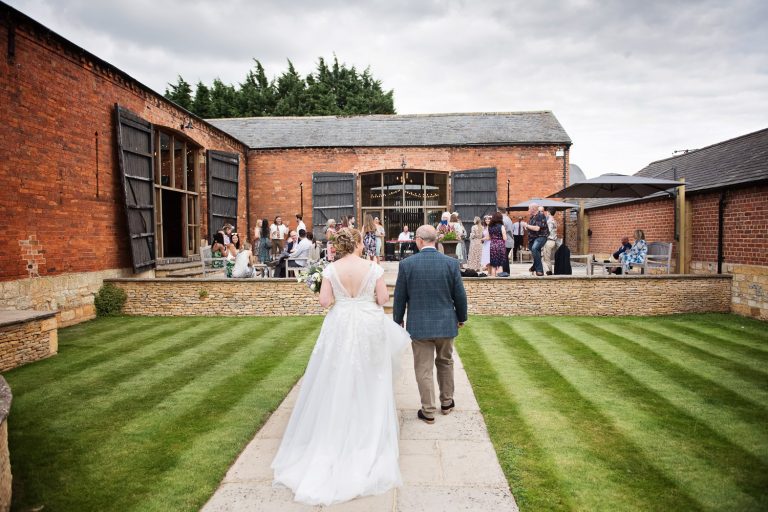 Back of bride and groom as they walk towards their wedding guests at Mickleton Hills Farm.