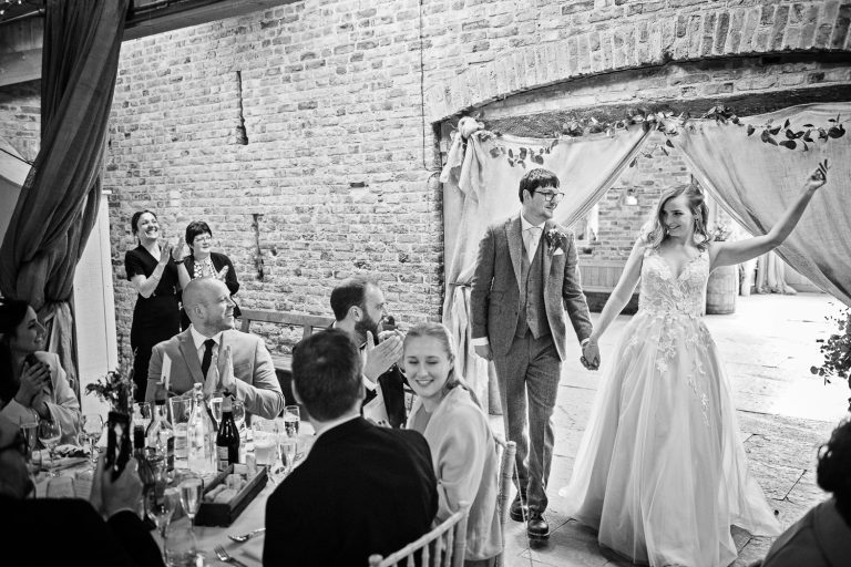 B&W photo of bride and groom entering the wedding barn to applause from family and friends.