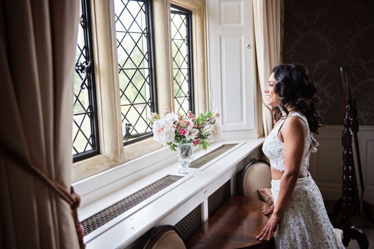 Bride wearing her white wedding dress, looks out of a gorgeous bay window.