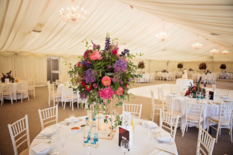 Wedding breakfast layout in the marquee at North Mymms Park. Large and colourful floral bouquets adjourn each table.