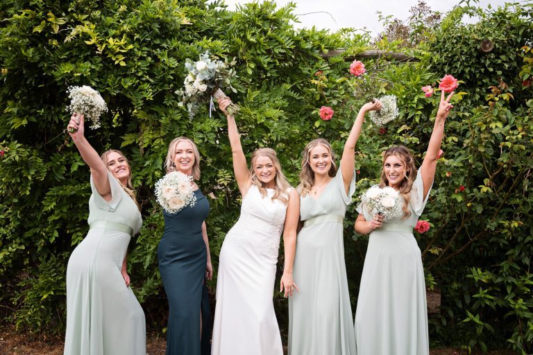 Bride and bridesmaids hold their wedding flowers in the air. Fun image.