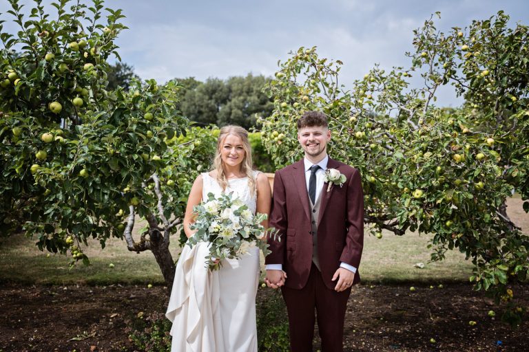 Bride and groom stand together in an apple orchard.
