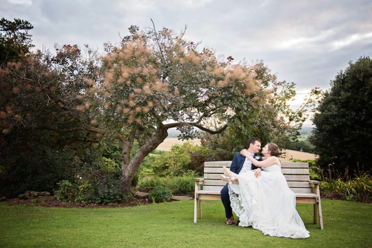 Bride and groom kiss on a bench.