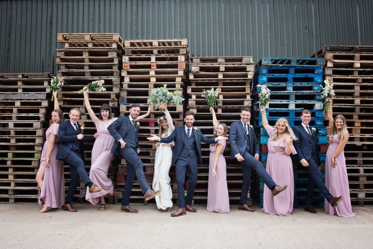 Bridal party striking poses next to wooden pallets. Looks fun. In Gloucester