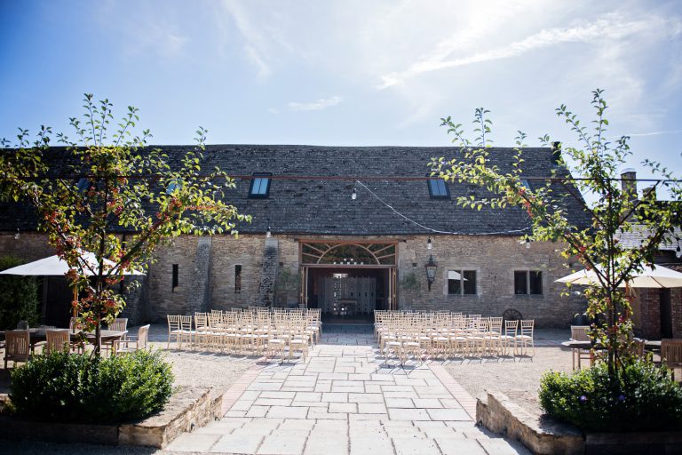 Overview of an outdoor ceremony next to a Cotswold barn.