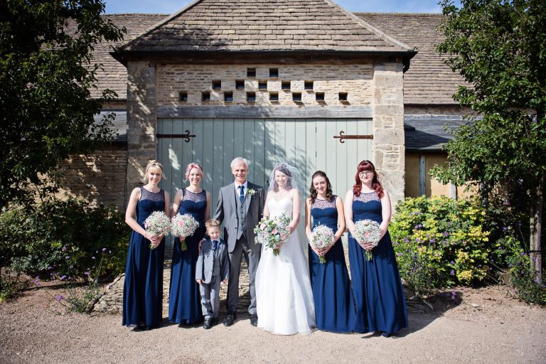 Bridesmaids, bride and father of the bride pose outside a dovecote before the wedding ceremony.