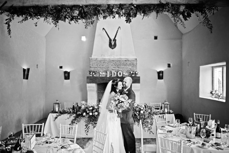 B&W image of bride and groom laughing in the wedding breakfast area at Oxleaze Barn.