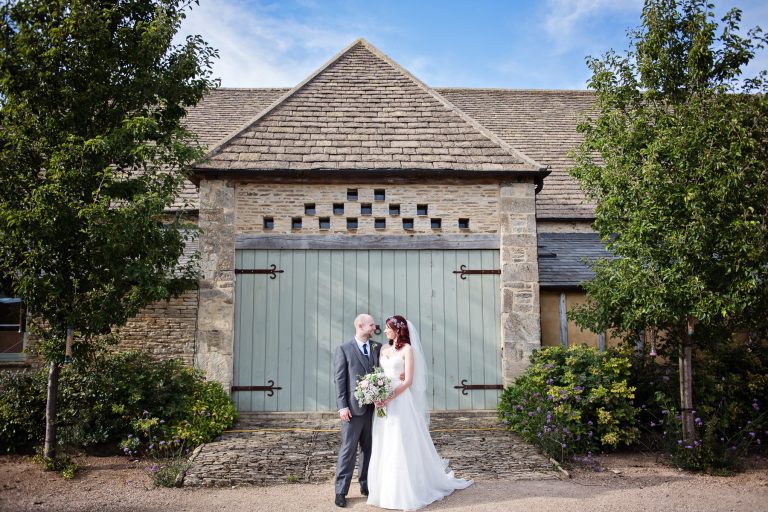 Bride and groom stand in front of a old yet modern barn with Dovecotes as an interesting feature.