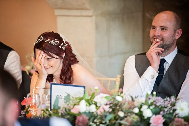 Canid photo of Bride putting her hand over half her face as she listens to some of the wedding speech.