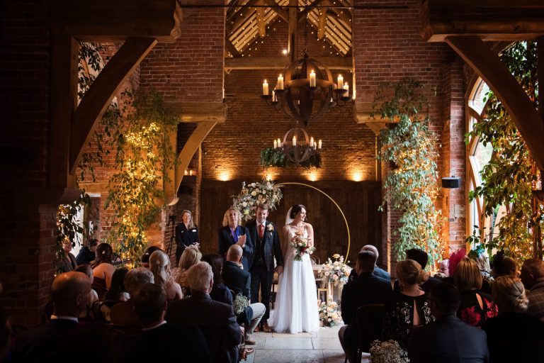 Bride and groom plus all the wedding guests at the end of their wedding ceremony in an old barn.
