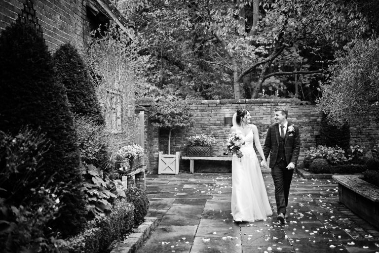 B&W image of a bride and groom holding hands and walking together. Candid photo