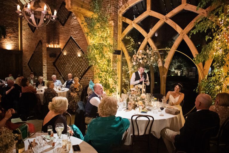 Natural, unposed photo of Groom making his wedding speech in front of family and friends. Beautiful uplighting.