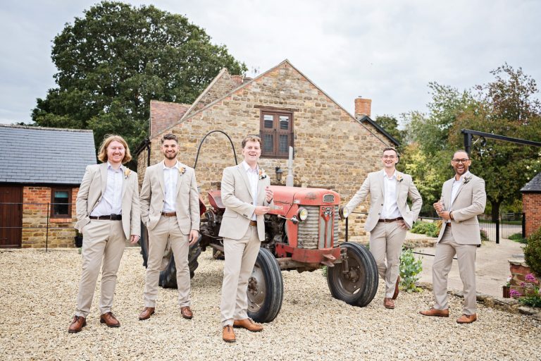 Groomsmen stand apart next to a very old tractor.