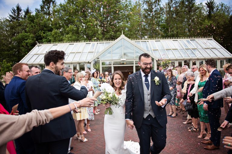 Candid, storytelling photo of bride and groom being showered with confetti as they walk down the wedding isle.