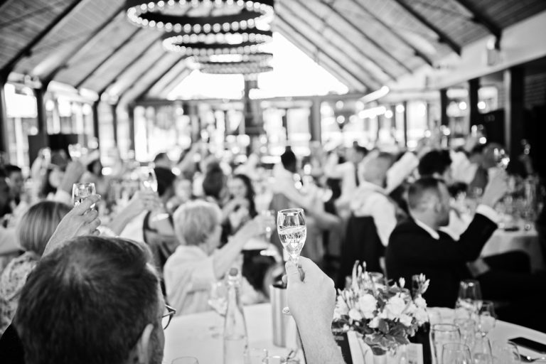 B&W documentary photo taken at Syrencot of wedding guests raising their glasses at the end of speeches.