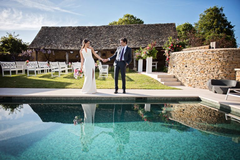 Bride and groom share a moment together by a Cotswold swimming pool. The couples reflection is in the swimming pool.