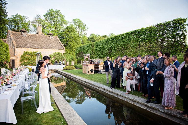 Relaxed photo of bride and groom being serenaded by their wedding guests in the garden.