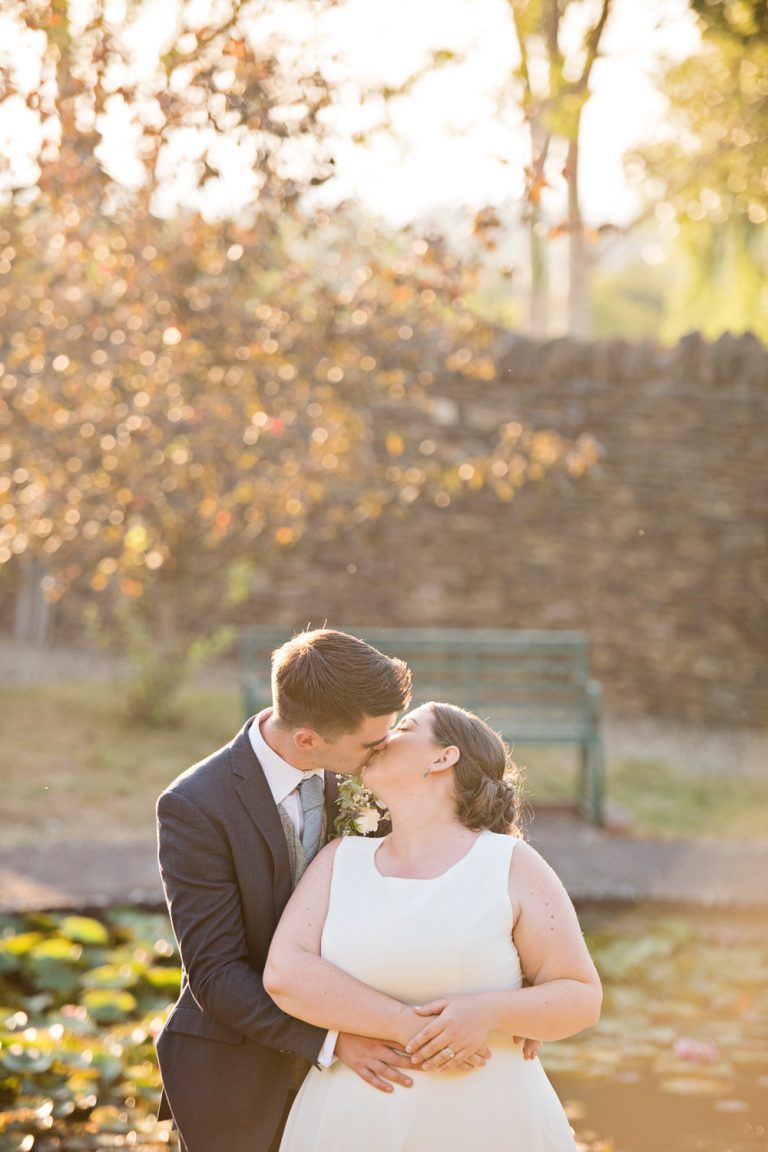 Natural photo of a bride and groom kissing by a pond during golden hour.