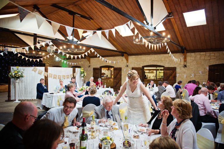 A candid photograph of the bride walking around the wedding tables chatting to guests.