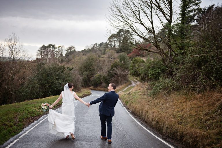 Bride and groom walking along the road (away from camera) hand in hand after getting married