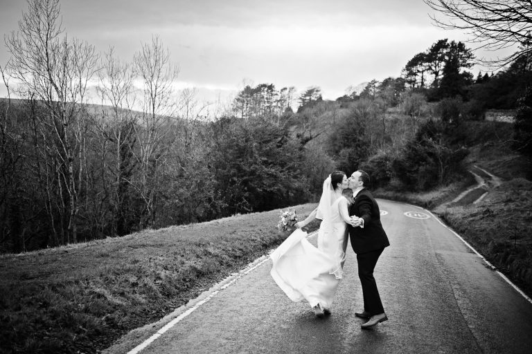 B&W photo of bride and groom kissing in the middle of a road.