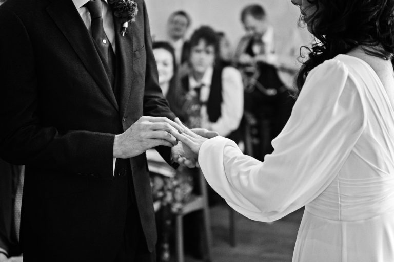 B&W candid photo of bride and groom exchanging their wedding rings at a wedding ceremony in Bristol.
