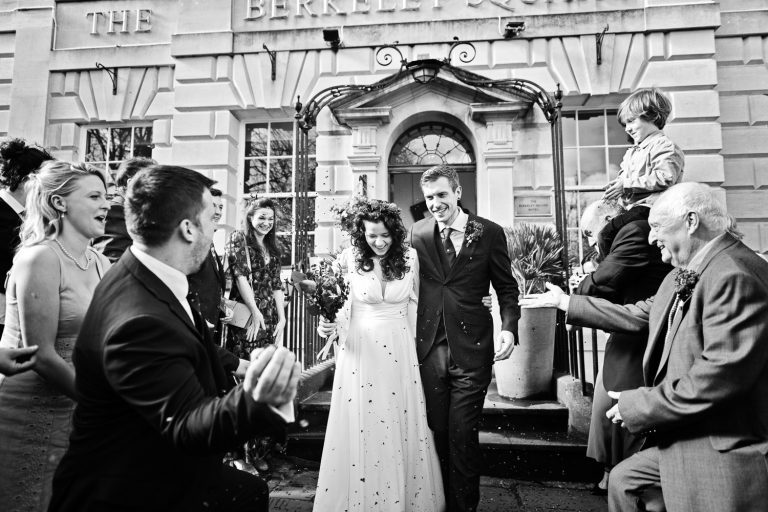 Documentary photo of bride and groom exiting The Berkeley Square Hotel after their wedding with their close friends and family throwing confetti at them.