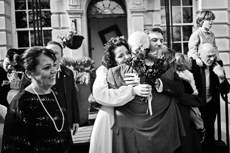 B&W candid photo of bride and groom being hugged by the grooms father. Classic documentary styled photo of a wedding in Bristol.