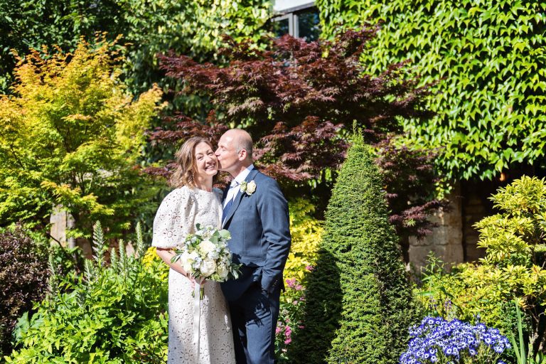 Groom kissing the bride on the cheek in the summer gardens at Lygon Arms Broadway.