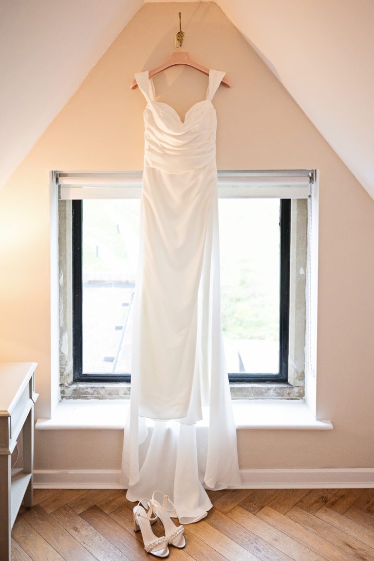 Wedding dress hung up in a pitched roof in front of a window.