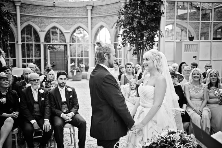 Bride and groom say their wedding vows with their wedding guests watching. B&W photo.