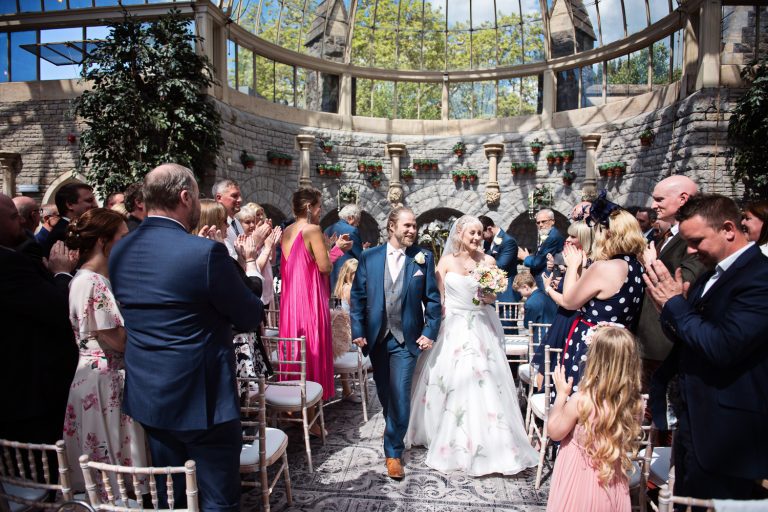 Bride and groom walk down the wedding isle in the Orangery at Tortworth Court.