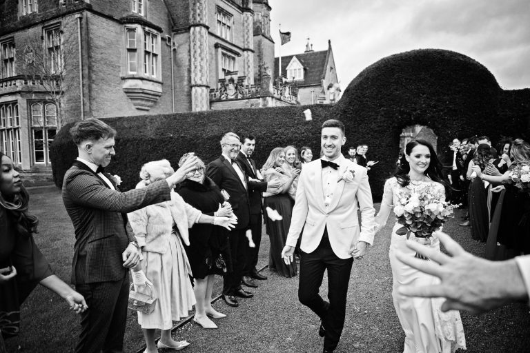 B&W candid photo of Bride and groom getting showered by confetti.