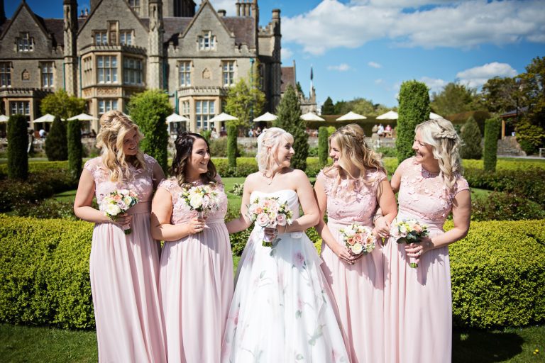 Bride and bridesmaids smiling at each other in the formal grounds of this wedding venue.