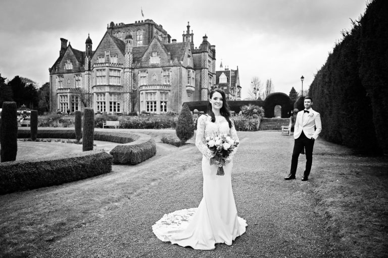 Formal b&w photo of bride and groom standing apart but with Tortworth Court behind them.