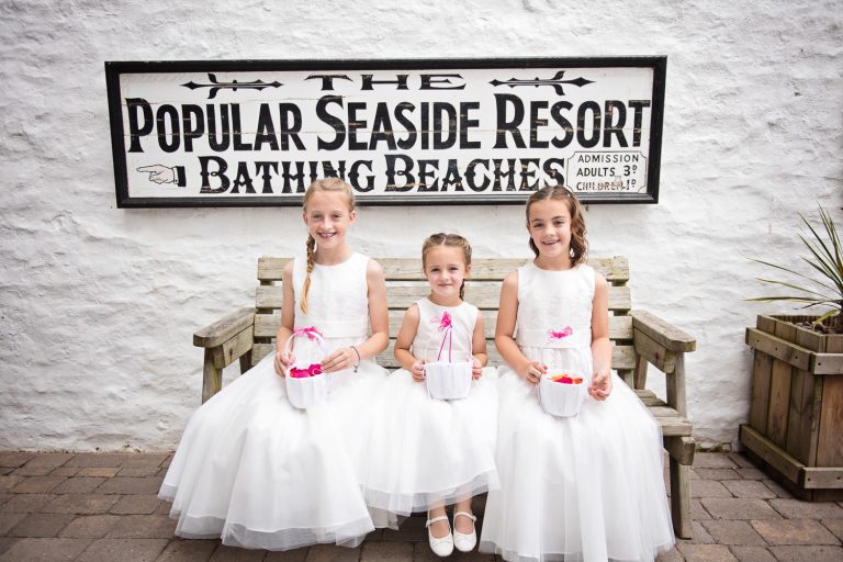 Flower girls sit on the bench at Tunnel Beach. The sign reads "The Popular Seaside Resort, Bathing Beaches"