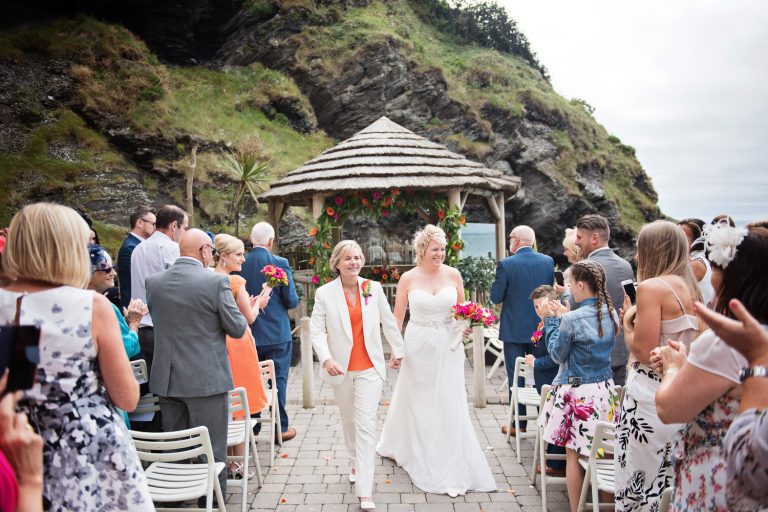 Bride and bride walk down the wedding isle with their wedding guests clapping and cheering.