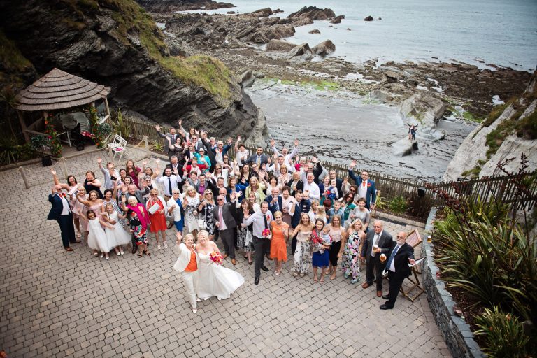 Large group photo of everyone at the wedding at Tunnel Beach. You can also see the sea and rocks.