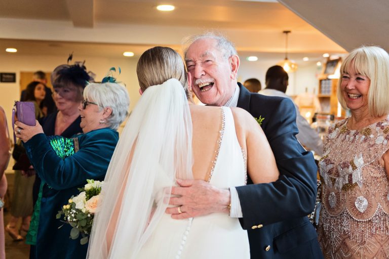 Natural candid photo of bride being hugged by her grandfather.