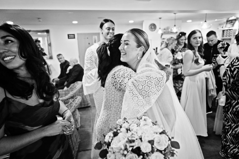 B&W candid photo of bride being hugged by her wedding guests.