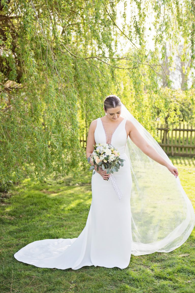 Bride plays with her veil by a willow tree.