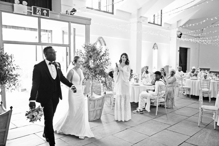 B&W photo of bride and groom making their entrance to Worton Hall. Wedding guests clapping.