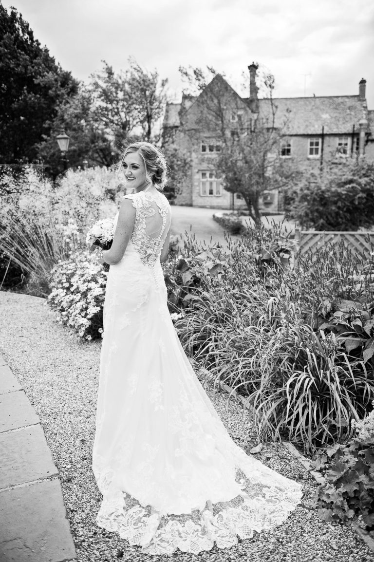 Portrait b&w photo of bride in her long wedding dress in the gardens at Hyde.