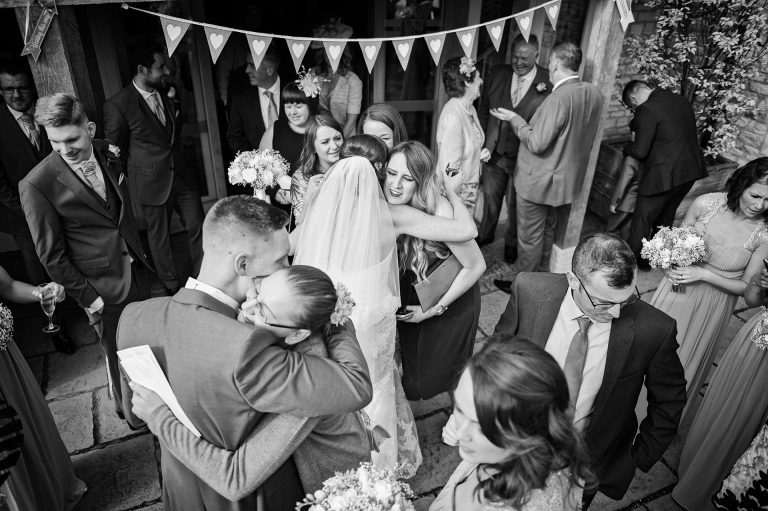 Candid storytelling photo of bride and groom getting congratulated by their wedding guests. B&W