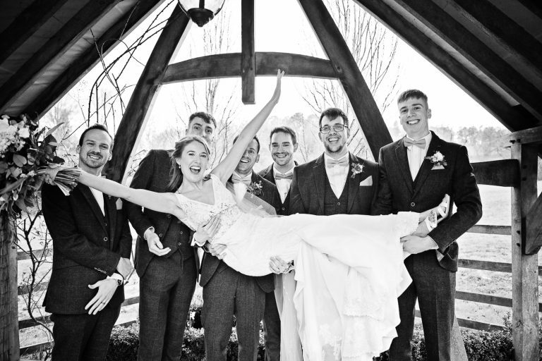 B&W photo of groomsmen carrying the bride.