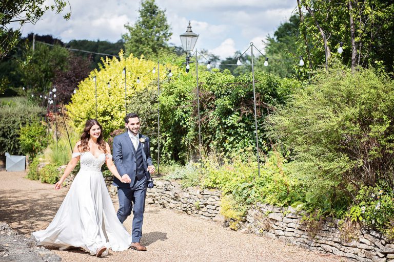 Bride and groom walk hand in hand smiling.