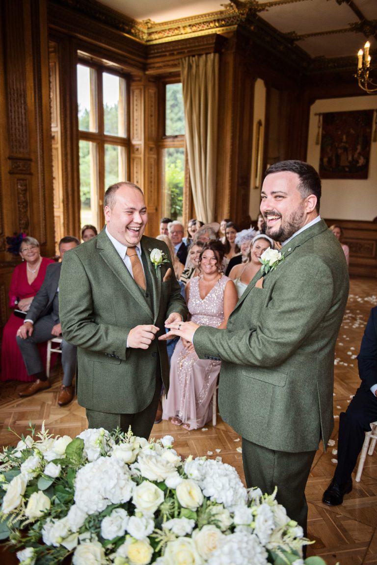 Portrait documentary photo of two grooms exchanging rings during their wedding ceremony.