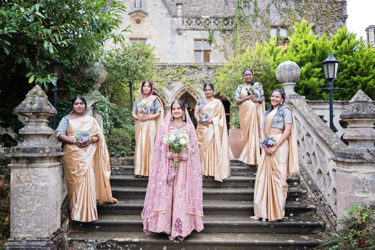 Bride and Bridesmaids dressed in Indian sari stand on the steps at Manor by the Lake.