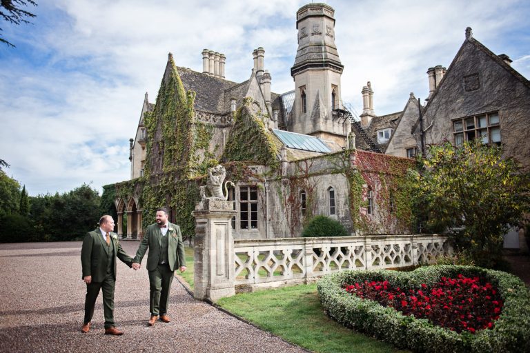 Groom and groom hold hands and walk outside the front of the impressive Manor By The Lake.
