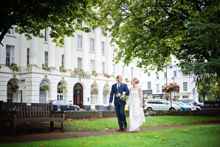 Exterior shot of the Queens Hotel with the bride and groom candidly walking in Imperial Gardens.